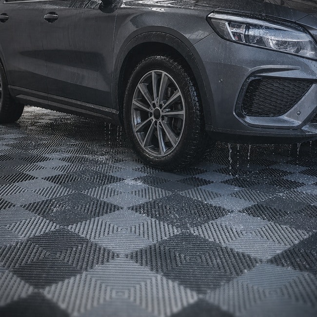 Grey and black interlocking garage floor tiles installed beneath a vehicle.